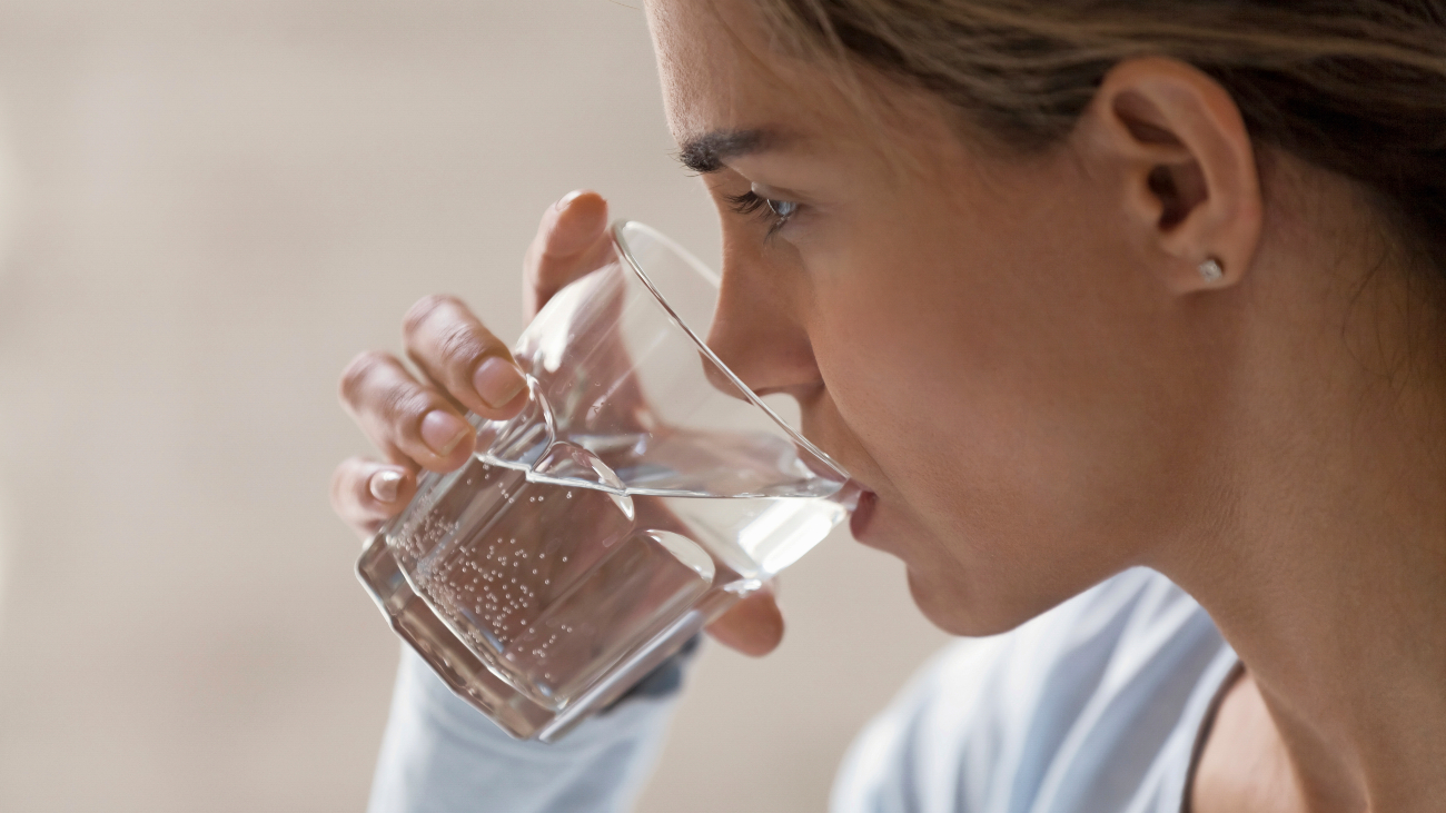 Vrouw drink glas water. Heeft ze dorst omdat ze knoflook heeft gegeten?