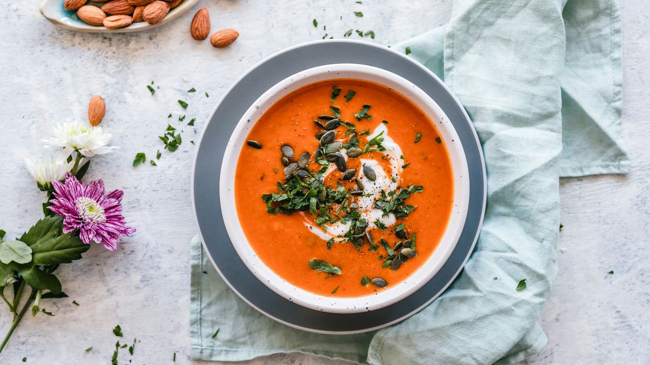 Een kom tomatensoep met noten en een bloem ernaast